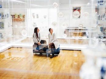 GRASSI Museum für Angewandte Kunst - Von Jugendstil bis Gegenwart Zwei Frauen Sitzen inmitten gläserner Vitrinen mit Ausstellungsstücken wie Tellern und Kannen im GRASSI Museum für Angewandte KunstTwo women sitting amid glass display cases with exhibits such as plates and jugs in the GRASSI Museum of Applied ArtsDvě ženy sedící uprostřed skleněných vitrín s exponáty, jako jsou talíře a džbány, v Muzeu užitého umění GRASSI.Dwie kobiety siedzące pośród szklanych gablot z eksponatami takimi jak talerze i dzbany w Muzeum Sztuki Użytkowej GRASSITwee vrouwen zitten te midden van glazen vitrines met tentoongestelde voorwerpen zoals borden en kannen in het GRASSI Museum of Applied ArtsDue donne sedute in mezzo a vetrine con oggetti esposti come piatti e brocche nel Museo di Arti Applicate GRASSI