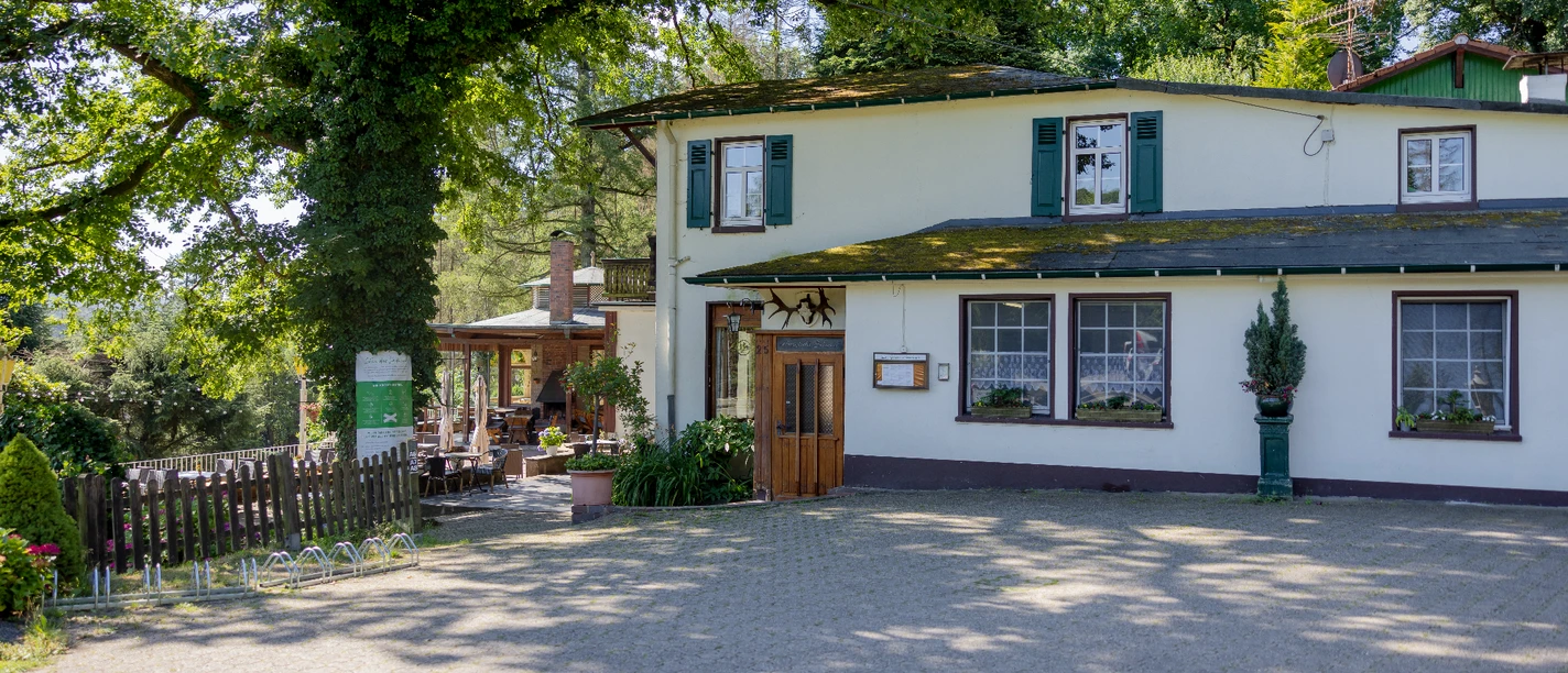 Bergische Schweiz Zweistöckiges weißes Gasthaus im Grünen, umgeben von Bäumen. Elegante Terrasse im Hintergrund.