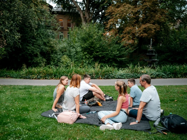 Family sits on a blanket in Einbeck Abbey Gardens and enjoys a break together in the greenery
