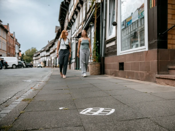 Einbecker Bierpfad Zwei Personen laufen auf einem Bürgersteig in der Einbecker Innenstadt, auf dem Boden ein aufgemaltes Bierfass des Einbecker Bierpfades.