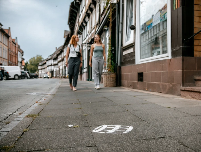 Einbecker Bierpfad Zwei Personen laufen auf einem Bürgersteig in der Einbecker Innenstadt, auf dem Boden ein aufgemaltes Bierfass des Einbecker Bierpfades.