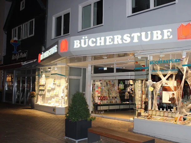 Lübbecker Bücherstube.JPG Leuchtende Buchhandlung mit offener Glastür, Schaufenstern voller Bücher in der Abenddämmerung.
