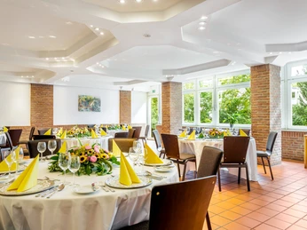 Kolpingsaal Messehotel Gefliester Konferenzraum mit Bankettbestuhlung, gedeckten Tischen mit Blumendeko und Blick in die NaturTiled conference room with banquet seating, laid tables with floral decorations and a view of nature