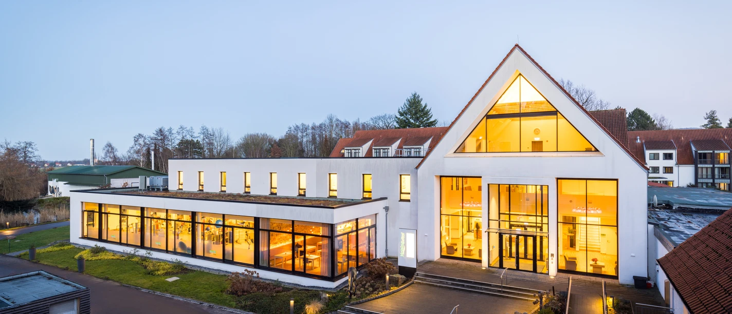 HolsingVital - Außenansicht erleuchtet Außenansicht der Reha-Klinik HolsingVital bei leichter Dämmerung, das Haus ist von innen beleuchtet