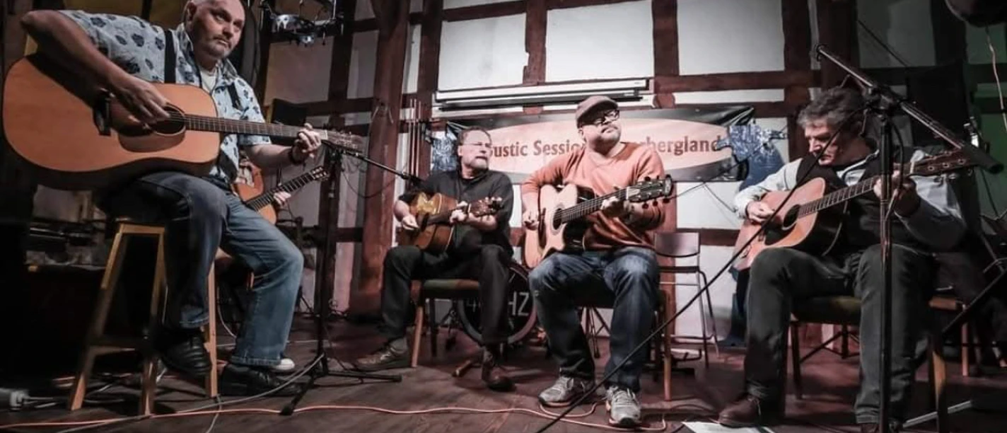 Vier Musiker mit Akustikgitarren spielen auf einer Bühne, umgeben von einem Fachwerk im Hintergrund.
