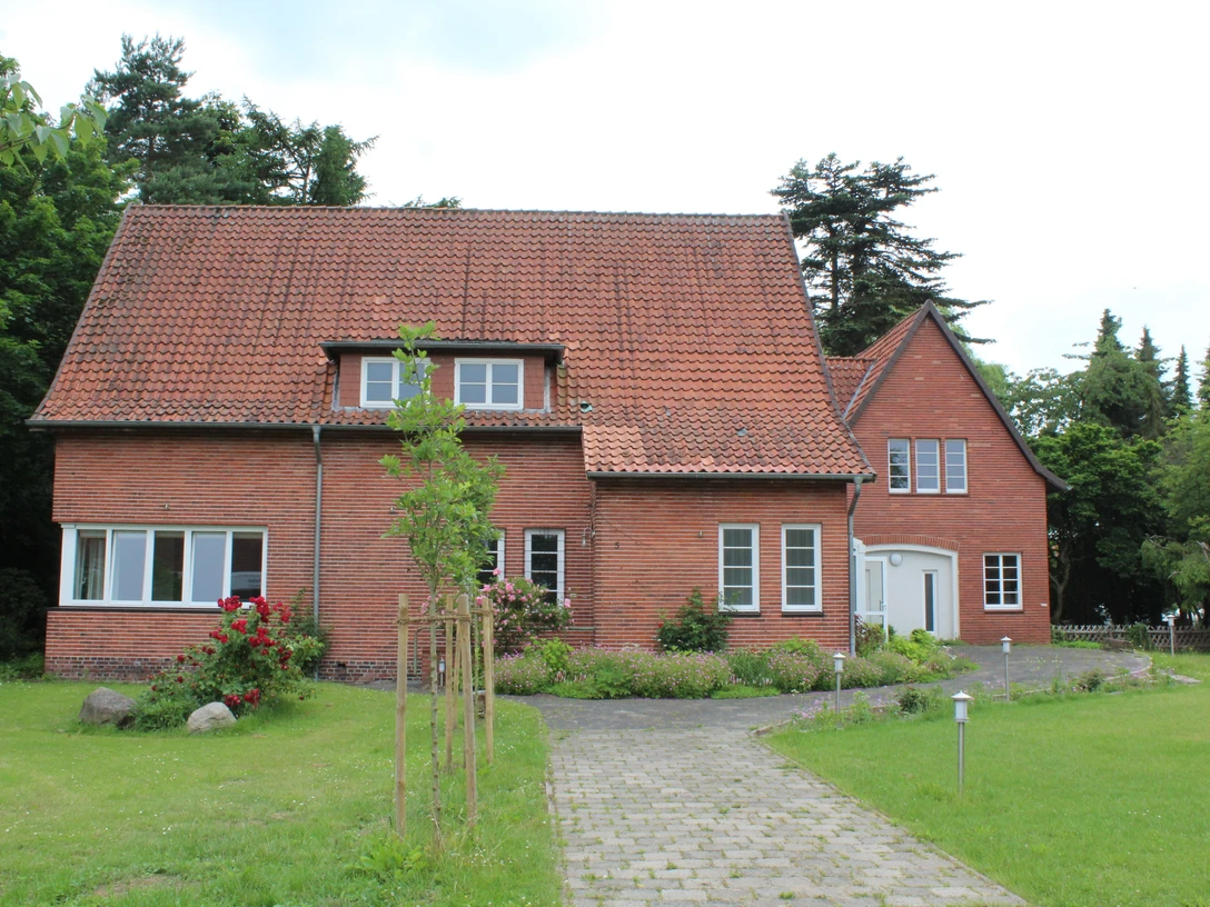 Binderhaus Rodewald Ein rotes Backsteinhaus mit Satteldach steht inmitten einer grünen Wiese, umgeben von hohen Bäumen.