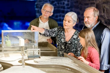 LVR-Industriemuseum Kraftwerk Ermen & Engels Älteres Paar und Kinder betrachten interessiert ein Architekturmodell in einem Museum oder Ausstellungsraum.