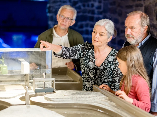 LVR-Industriemuseum Kraftwerk Ermen & Engels Älteres Paar und Kinder betrachten interessiert ein Architekturmodell in einem Museum oder Ausstellungsraum.