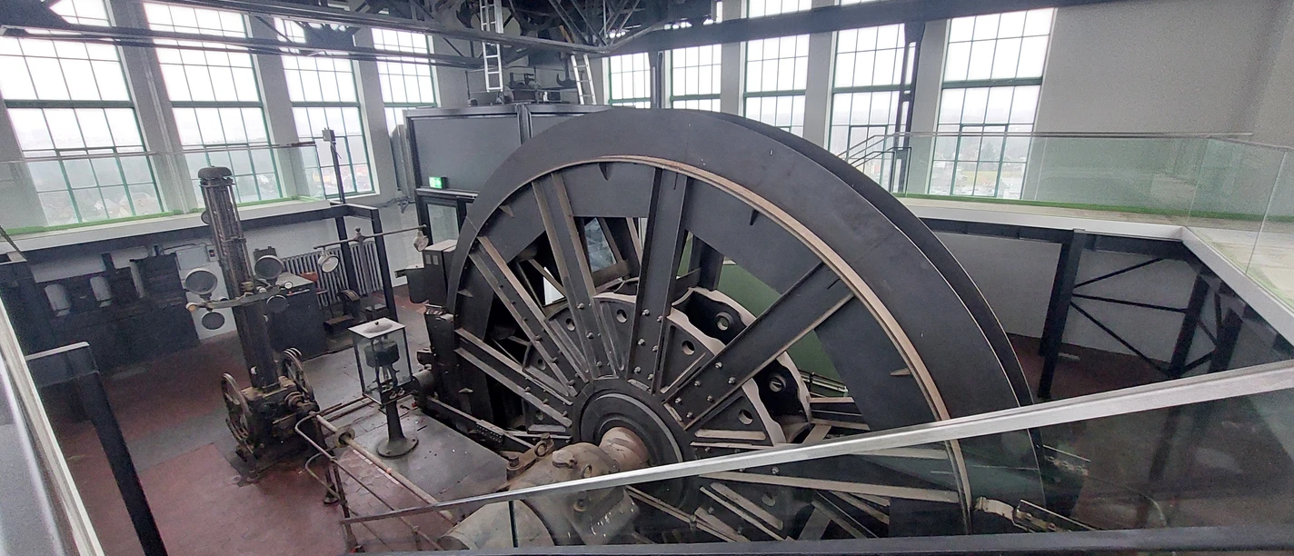 20250123_121118.jpg Historische Industriemaschine in einem lichtdurchfluteten Gebäude mit großen Fenstern.