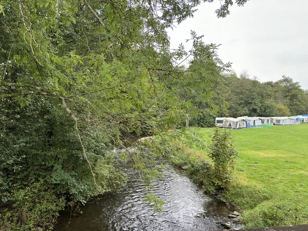 Blick auf einen kleinen Bach, der an grünen Wiesen und einem Zeltplatz vorbeifließt.