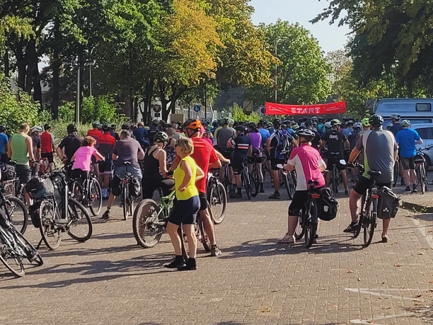 Radfahrer versammeln sich bei einem Startpunkt für eine Tour auf ländlicher Straße mit rotem Banner.