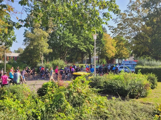 Eine große Gruppe von Radfahrern versammelt sich bei sonnigem Wetter im Grünen für die Sieben Pässe Tour.