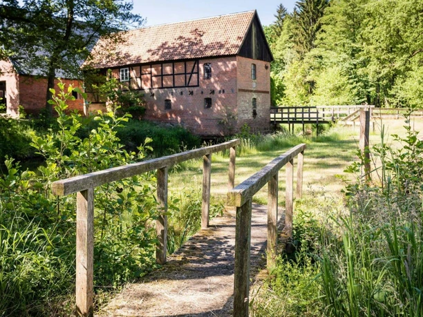 Mühle mit Brücke Holzbrücke über einen Bach, dahinter eine alte Mühle aus Backstein und Fachwerk.