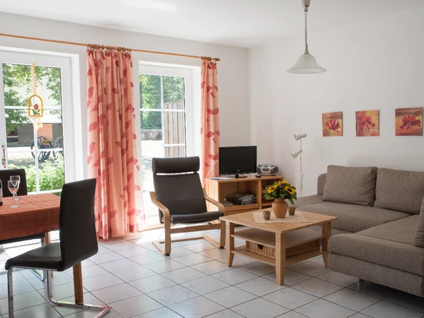 Helles Wohnzimmer mit grauem Sofa, Esstisch und Glastüren, die auf den Bauernhof führen.