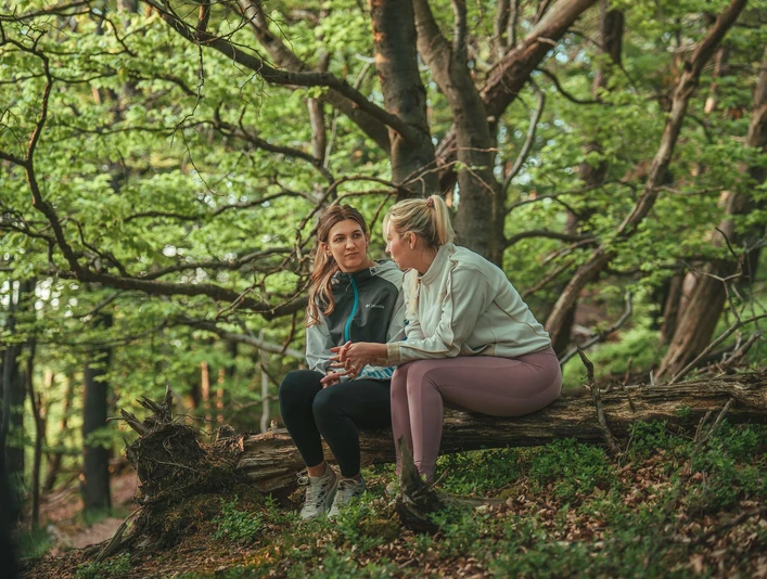 2 Frauen sitzen auf einer Baumwurzel im Buchenwald 2 Frauen sitzen auf einer Baumwurzel im Buchenwald