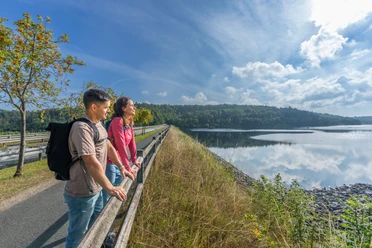 BadWuennenberg–Aabachtalsperre-027 ©Teutoburger Wald Tourismus, Patrick Gawandtka.jpg Zwei Personen genießen die ruhige Aussicht auf einen großen Stausee mit umliegendem Waldgebiet.