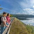 BadWuennenberg–Aabachtalsperre-027 ©Teutoburger Wald Tourismus, Patrick Gawandtka.jpg Zwei Personen genießen die ruhige Aussicht auf einen großen Stausee mit umliegendem Waldgebiet.