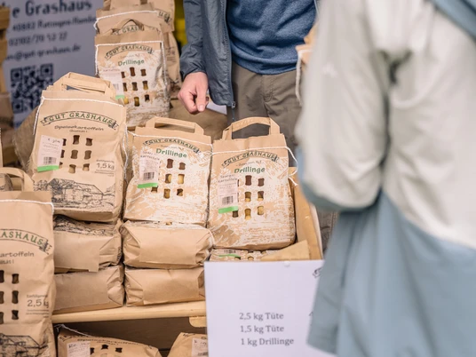 Kartoffeln im Verkauf von Gut Grashaus Verkauf von frischen Kartoffeln in Kartontüten auf einem Marktstand, präsentiert von Gut Grashaus.