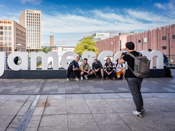 gamescom Sechs Personen posieren lächelnd vor einem großen "gamescom"-Schild, während ein Mensch sie fotografiert.Six people pose smiling in front of a large "gamescom" sign while a person photographs them.