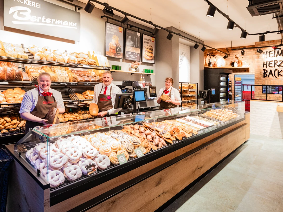 Das Bild zeigt den Tresenbereich einer Filiale mit den Verkaufsprodukten und drei Mitarbeitern.