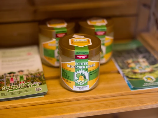 Biohof Mohme_Hofladen_ Honiggläser mit Aufschrift "Echter Deutscher Honig", umgeben von bunten Flyern in einem hölzernen Regal.