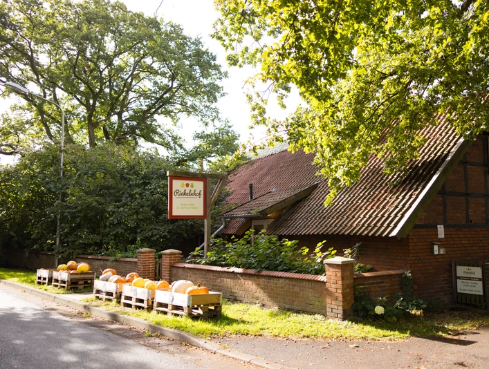 Riekelnhof Mosterei Riekelnhof Mosterei mit Fachwerk-Gebäude, Kürbiskisten und grünen Bäumen in ländlicher Umgebung.