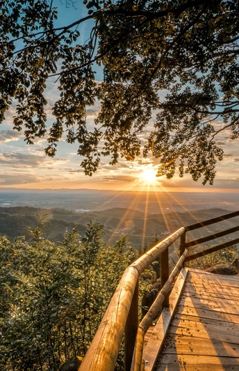 Bürstenstein. Eine Holzplattform unter einem Baum. Man schaut über Felsen und Berge in den Sonnenuntergang