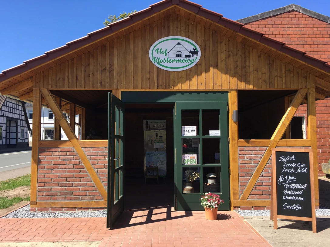 Hof Klostermeier Holzfassade mit offenem Tor und grüner Tür. Schild "Hof Klostermeier" über dem Eingang.