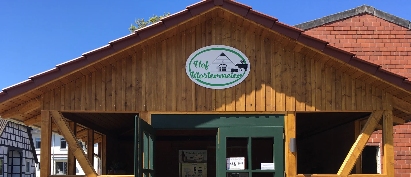 Hof Klostermeier Holzfassade mit offenem Tor und grüner Tür. Schild "Hof Klostermeier" über dem Eingang.