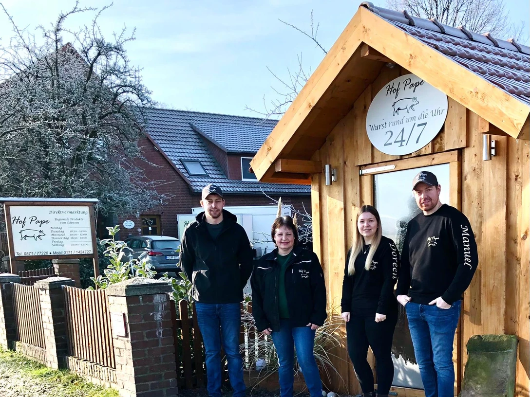 Hof Pape Vier Personen stehen lächelnd vor einem hölzernen Gebäude mit "Hof Pape"-Schild.