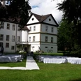 Weiß gedeckte Tische und Stühle stehen auf einer grünen Wiese vor einem historischen Schlossgebäude.