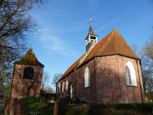 Kirche Jennelt Backsteinkirche mit separatem Glockenturm, spitzem Dach und weißen Spitzbogenfenstern im Sonnenlicht.