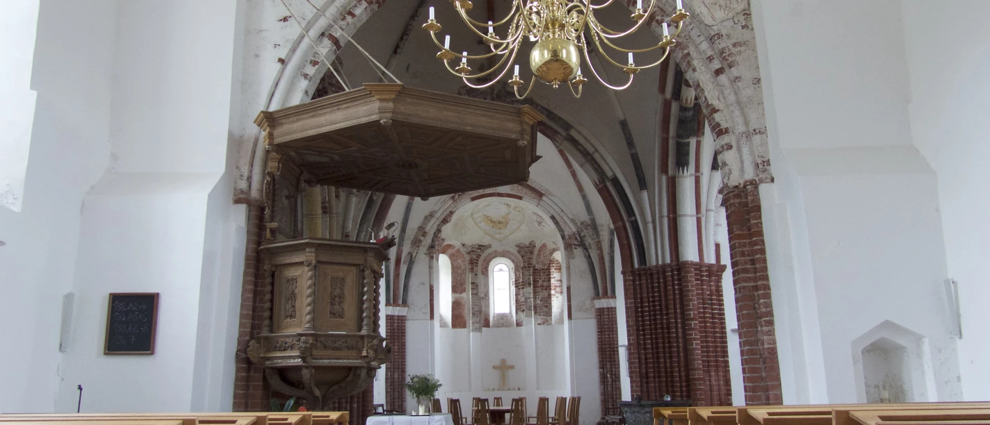 Kirche Pilsum Innenansicht der Kirche Pilsum mit Holzbänken, Kanzel und Kronleuchter unter einem Backsteingewölbe.