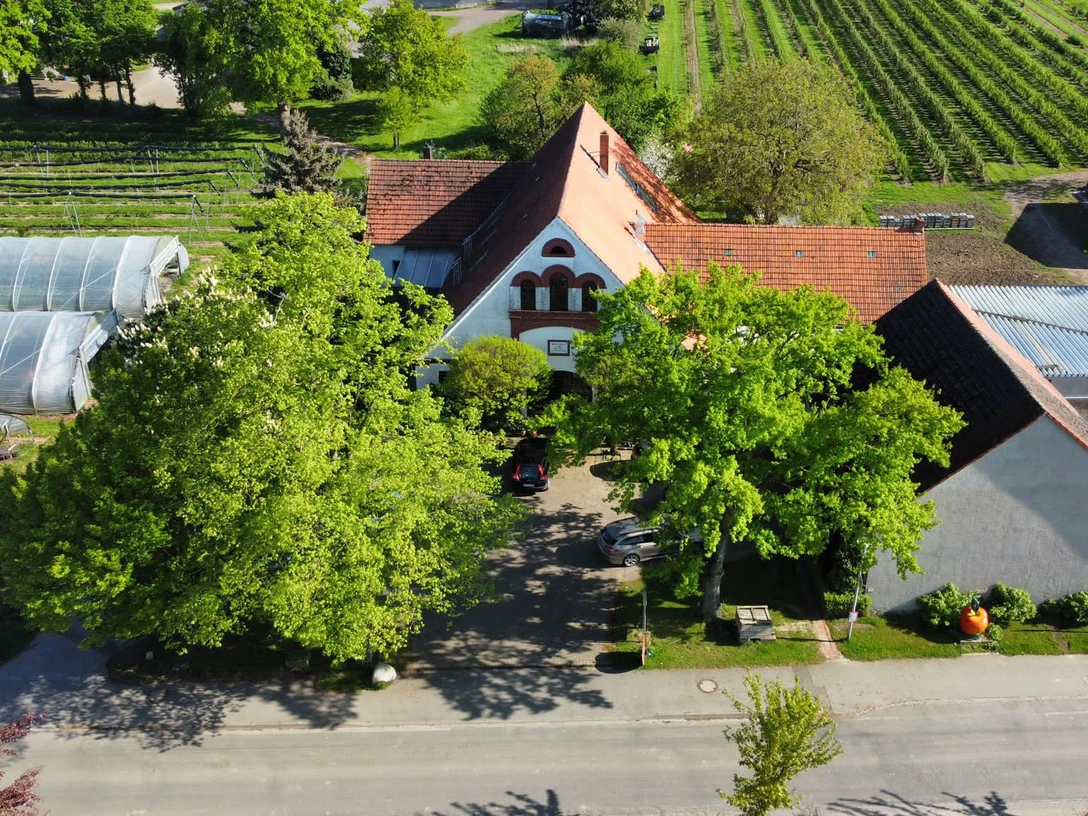 Obsthof Wickemeyer Luftaufnahme des Obsthofs mit Gebäude, umgeben von Gärten und Gewächshäusern, bei sonnigem Wetter.
