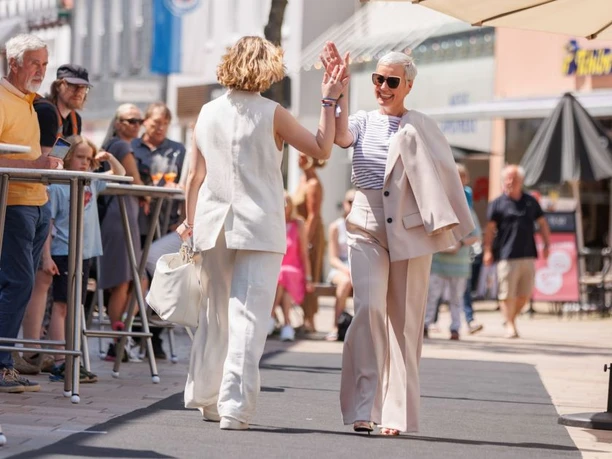 Zwei modisch gekleidete Frauen geben sich auf einem Laufsteg inmitten einer Menschenmenge ein High-Five.