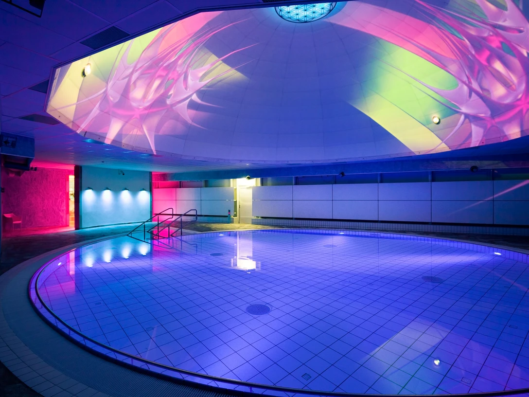 Liquid Sound Tempel Toskana Therme Beleuchtetes Hallenbad mit rundem Becken, blauen und pinken Lichtern sowie bunten Projektionen an der Decke, moderne und entspannte Atmosphäre.Illuminated indoor pool with round pool, blue and pink lights and colorful projections on the ceiling, modern and relaxed atmosphere.Osvětlený krytý bazén s kulatým bazénem, modrými a růžovými světly a barevnými projekcemi na stropě, moderní a uvolněná atmosféra.Podświetlany kryty basen z okrągłym basenem, niebieskie i różowe światła oraz kolorowe projekcje na suficie, nowoczesna i relaksująca atmosfera.Verlicht binnenzwembad met rond bad, blauwe en roze lichten en kleurrijke projecties op het plafond, moderne en ontspannen sfeer.Piscina interna illuminata con vasca rotonda, luci blu e rosa e proiezioni colorate sul soffitto, atmosfera moderna e rilassata.