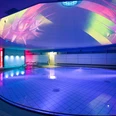 Liquid Sound Tempel Toskana Therme Beleuchtetes Hallenbad mit rundem Becken, blauen und pinken Lichtern sowie bunten Projektionen an der Decke, moderne und entspannte Atmosphäre.Illuminated indoor pool with round pool, blue and pink lights and colorful projections on the ceiling, modern and relaxed atmosphere.Osvětlený krytý bazén s kulatým bazénem, modrými a růžovými světly a barevnými projekcemi na stropě, moderní a uvolněná atmosféra.Podświetlany kryty basen z okrągłym basenem, niebieskie i różowe światła oraz kolorowe projekcje na suficie, nowoczesna i relaksująca atmosfera.Verlicht binnenzwembad met rond bad, blauwe en roze lichten en kleurrijke projecties op het plafond, moderne en ontspannen sfeer.Piscina interna illuminata con vasca rotonda, luci blu e rosa e proiezioni colorate sul soffitto, atmosfera moderna e rilassata.