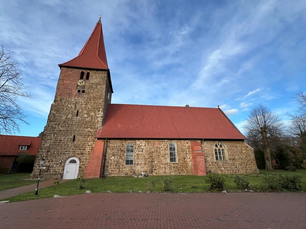 St. Bartholomäus Kirche Balge Eine historische Kirche mit rotem Ziegeldach und Steinmauern, umgeben von einem gepflasterten Gehweg.