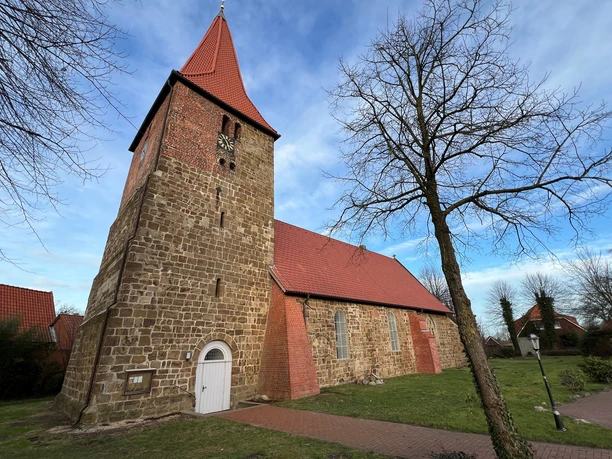 Eine historische Kirche mit einem hohen Glockenturm aus Backstein im Grünen von Balge.