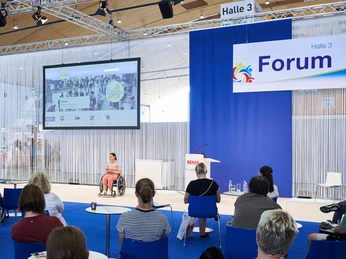 rehab_2022_messekarlsruhe_behrendt_rausch-510.jpg Besucher einer Messe in Karlsruhe, präsentiert wird ein Vortrag im Forum von Halle 3.