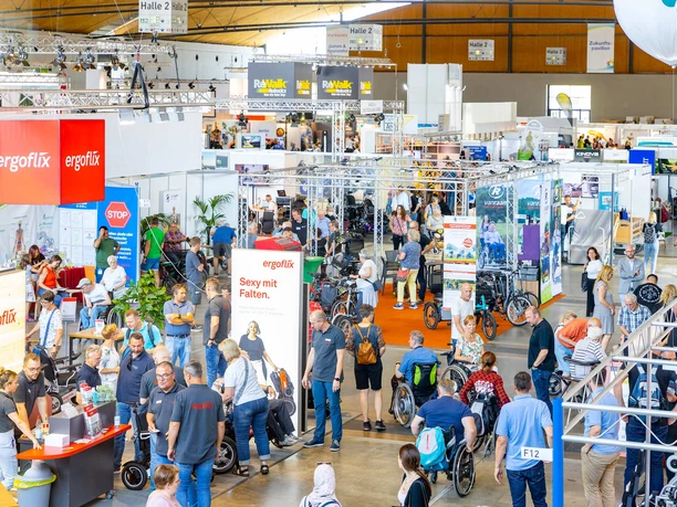 rehab_2023_messekarlsruhe_juergenroesner_284.jpg Voller Betrieb auf einer Messe mit vielen Ständen und Besuchergruppen.