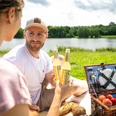 Espelkamp- See am Kleihügel Zwei Personen genießen ein Picknick am See, umgeben von Natur, mit Essen und Getränken im Freien.