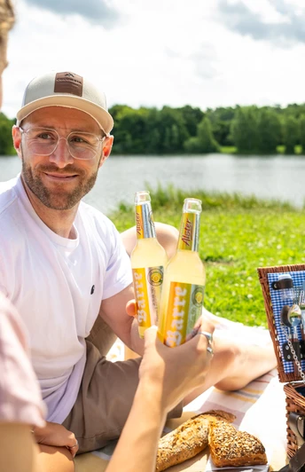 Espelkamp- See am Kleihügel Zwei Personen genießen ein Picknick am See, umgeben von Natur, mit Essen und Getränken im Freien.