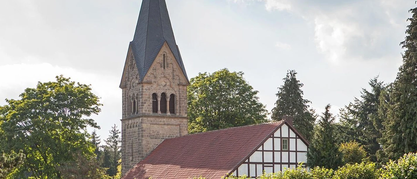 Evangelische Kirche Bergkirchen mit Fachwerk, Steinturm und Bäumen unter bewölktem Himmel