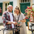 SIEBENECKEN.APP Ein lächelndes Paar erkundet mit Fahrrädern die Gegend. Sie betrachten gemeinsam eine Karte.