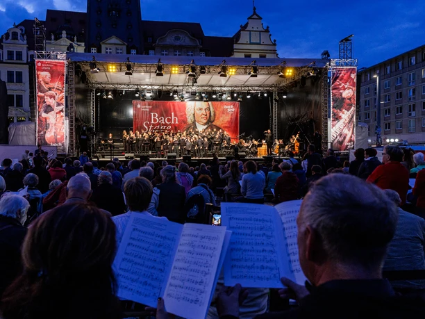 BF 24_BachStage1_Jens Schlüter.jpg Open-Air-Bühne mit Orchestermusikern bei einem Konzert, beleuchtet in der Abenddämmerung.