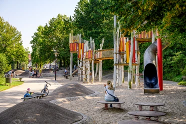 Wasserspielplatz Emssee Wiedenbrück 2 Moderner Spielplatz mit bunten Klettergerüsten, Rutsche und Sandfläche, umgeben von grünen Bäumen.