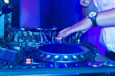 Nightlife Club Aachen Ein DJ legt im Nachtclub Platten auf, während bunte Lichter die Mischpulte beleuchten.