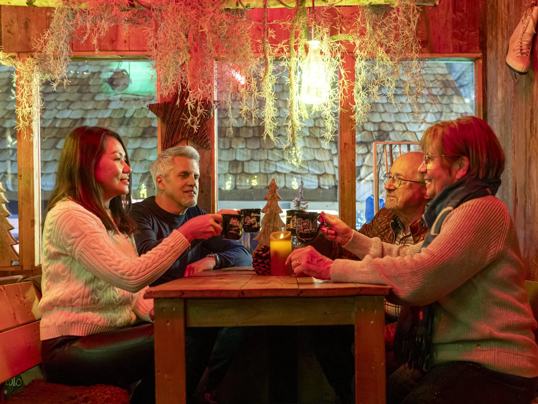 Weihnachtsmarkt 2024_Hütte_sitzend_gemütlich_Gruppe_Glühwein_anstoßen_2_Querformat_Ch. Bierwagen_CC-BY WEB.jpg