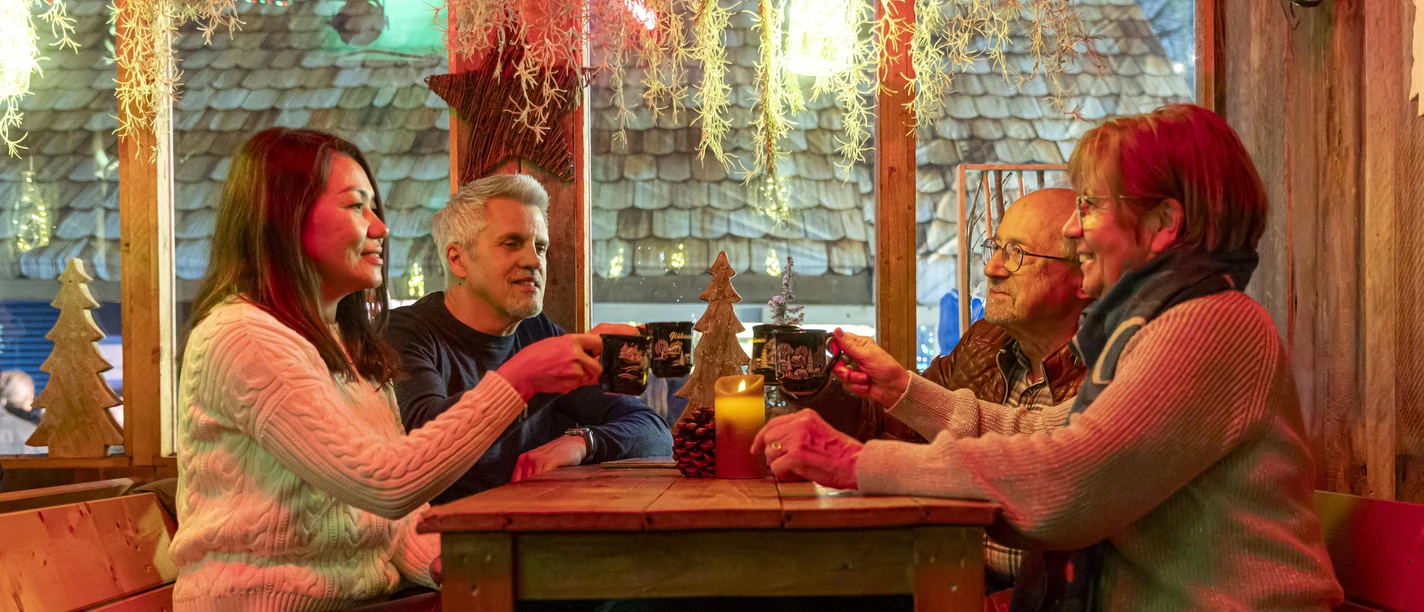 Weihnachtsmarkt 2024_Hütte_sitzend_gemütlich_Gruppe_Glühwein_anstoßen_2_Querformat_Ch. Bierwagen_CC-BY WEB.jpg